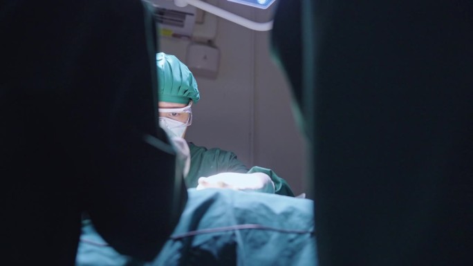 在手术室里，一名护士将手术刀递给一名男性外科医生，一名助手用纱布垫帮助他吸收病人手术伤口上的血液。