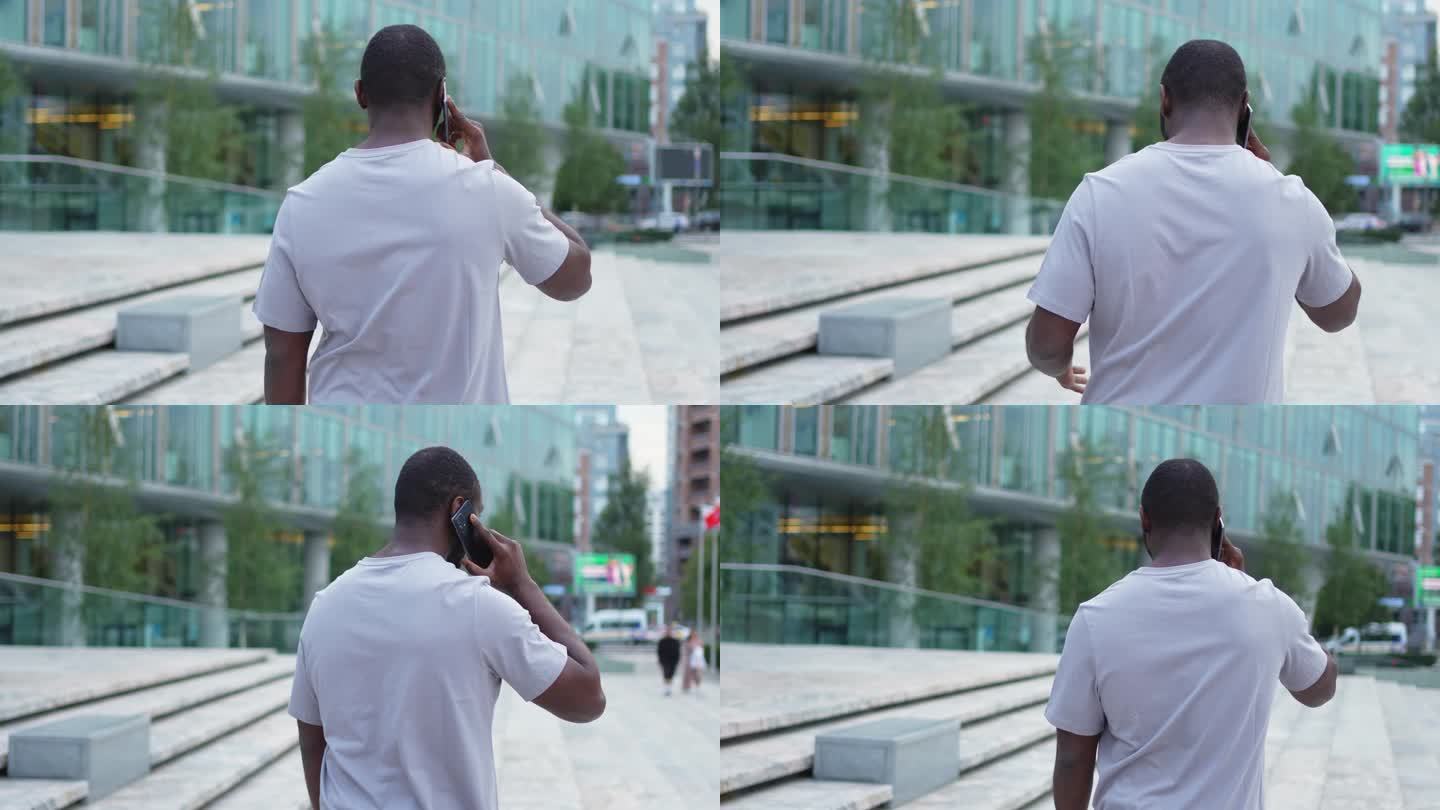 一个非洲裔美国人在户外用智能手机聊天。一个不认识的人，一个拿着手机的人走在城市的街上。男人用手机接电