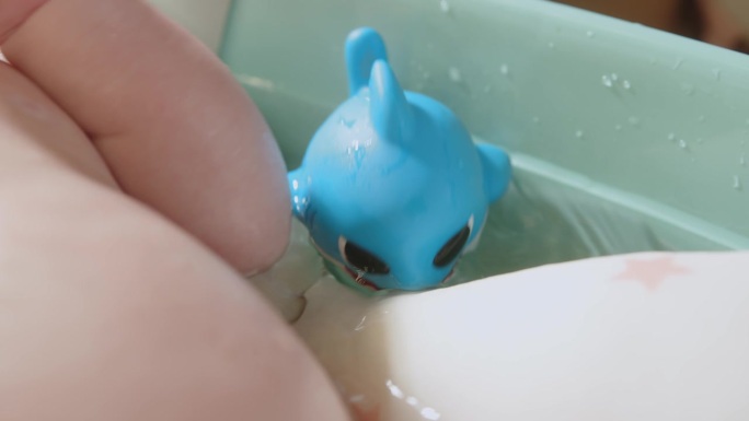 一个橡胶蓝鲨娃娃和一个新生婴儿在浴缸里。一个孩子在。一个有玩具鱼的浴缸。
