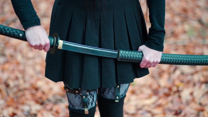 年轻的女孩穿着黑色的裙子，带着吊袜带和长袜，抽出一把武士刀。准备战斗。以五彩缤纷的秋叶为背景。闪亮的