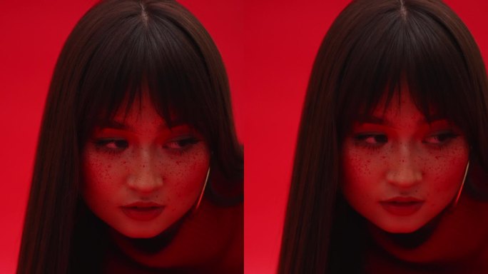 满脸雀斑的亚洲女孩在红色背景下看镜头的特写。垂直视频。艺妓模型