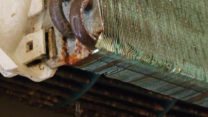 旧脏空调室内机散热器特写，上面有铜管、铜板和水滴。
