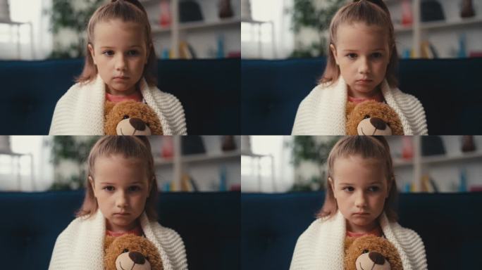 不开心的小女孩抱着泰迪熊独自坐在沙发上，悲伤