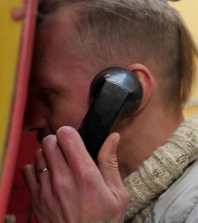 垂直视频:快乐迷人的男子使用街道公用电话亭拨打电话，同时保持匿名，不确认来电者的身份。用经典拨号电话