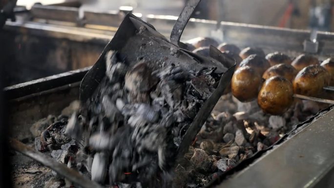特写一个装满热炭的钢勺，把煤倒进烤架里，用来煎烤串、烤羊肉串和烤土豆。用热煤煎肉