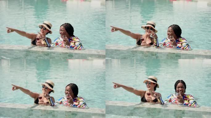 非洲女人和西班牙人，亲密的朋友，两个多民族的人站在水里喝着酒，愉快地聊天。在炎热的晴天里，在游泳池里
