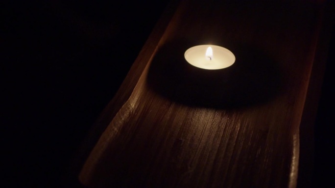 浓黑的房间里，单支茶烛在浓黑的棕色木盘里燃烧