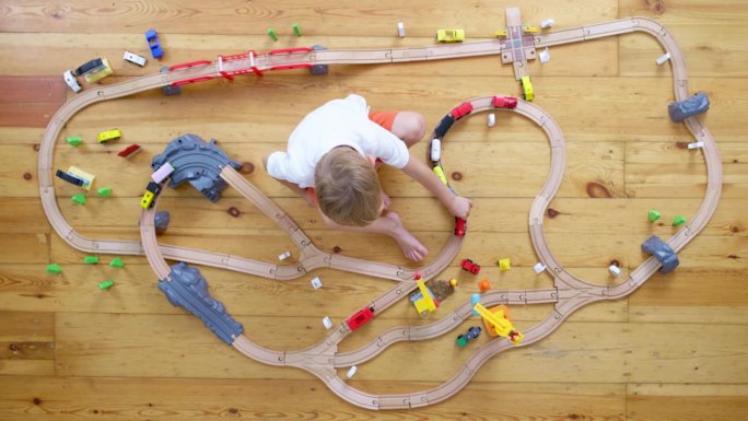 可爱的孩子在家里或幼儿园的地板上玩木制铁路玩具。俯视图