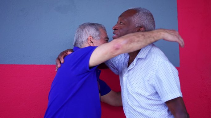 两个不同肤色的老年人站在街上互相拥抱。一个黑人老人拥抱他的白人朋友，描绘老年友谊