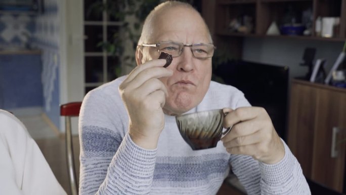 一位老人一边喝茶一边吃巧克力