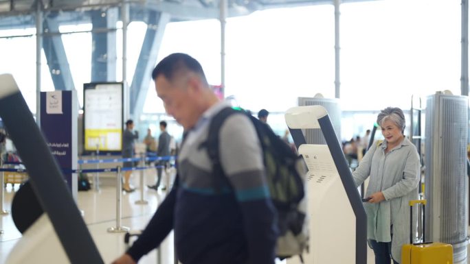 4K亚洲老人在机场候机楼的机器上自助办理登机手续。