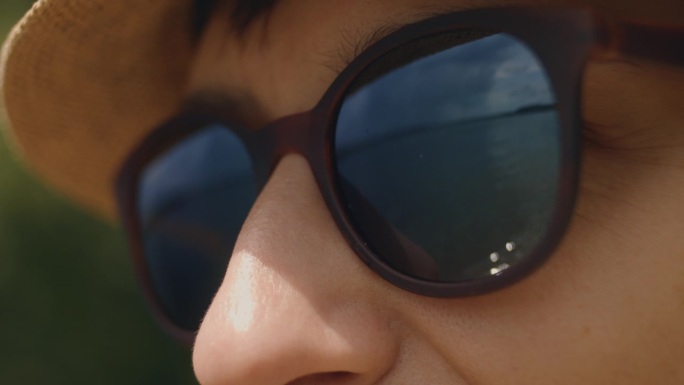 一个快乐的年轻黑发女人带着帽子和太阳镜在海滩度假的慢镜头特写