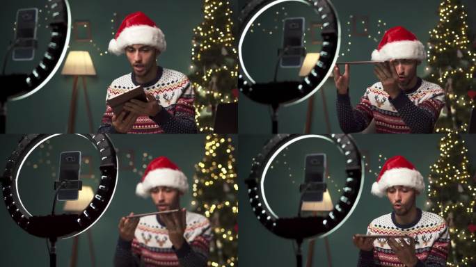 年轻的阿拉伯男博主在圣诞节用智能手机相机上的数码平板电脑打开包裹，为科技博客录制视频内容。假期和科技
