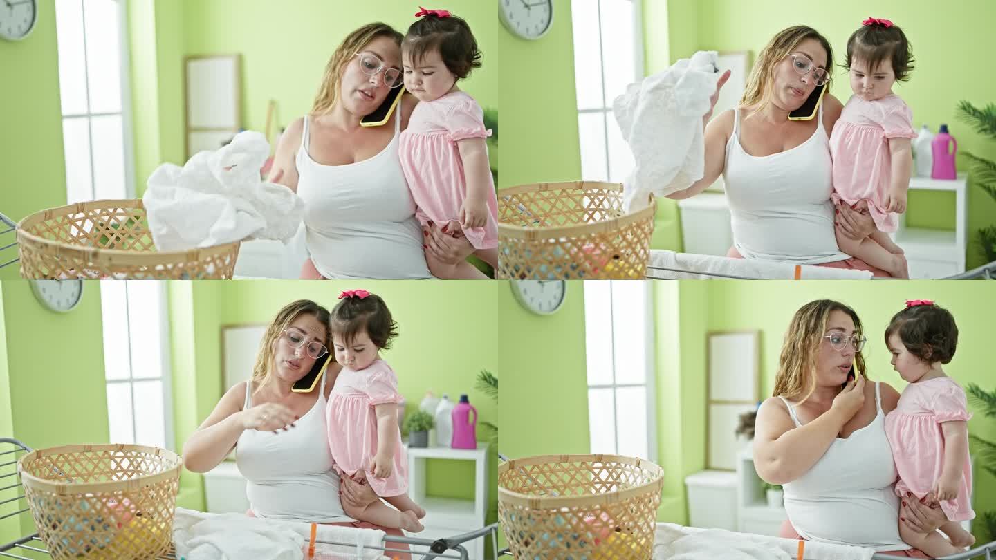 可爱的妈妈抱着她的宝贝女儿，一边讲着手机，一边悠闲地把衣服挂在晾衣绳上，享受着家里洗衣房的日常琐事