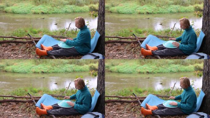 一位音乐家在演奏葡萄糖衣机。一个人在河边的秋天公园里。敲击乐器穿越森林的旅程