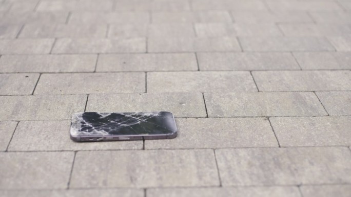 智能手机在人行道上摔了一跤，一名男子拿着一个坏了屏幕的智能手机捡了起来