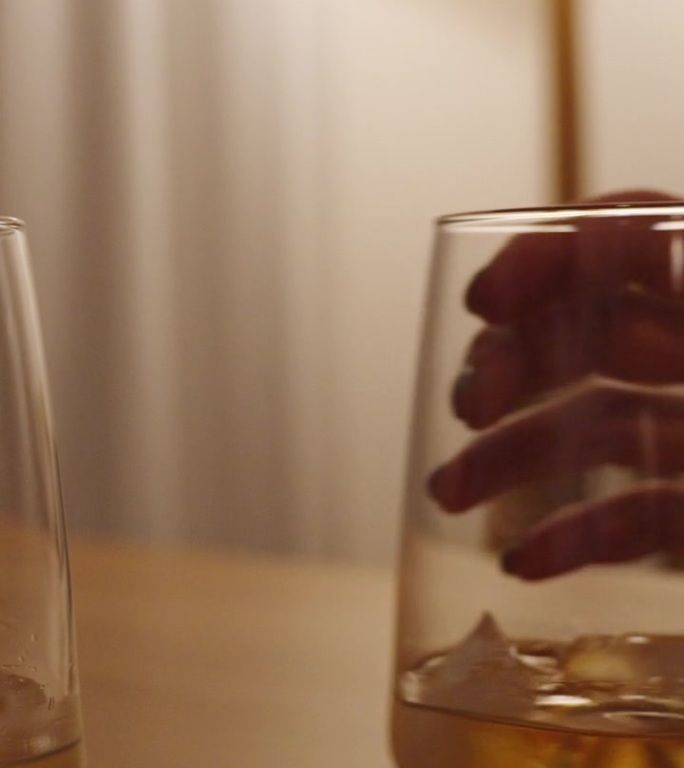 垂直视频。男人和女人把他们的威士忌酒杯并排放在一张木桌上。这个场景是在一个白色的房间里被昏暗而温暖的