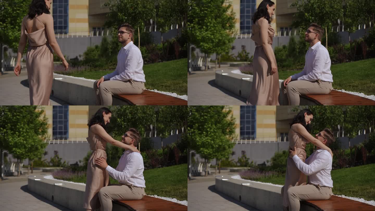 一个男人坐在公园的长椅上遇见了他的爱人。一个女人走过来拥抱了一个坐着的男人。