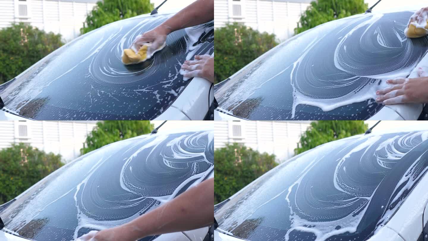 用泡沫洗发水和水喷雾洗车的男子的手。汽车保养和清洁