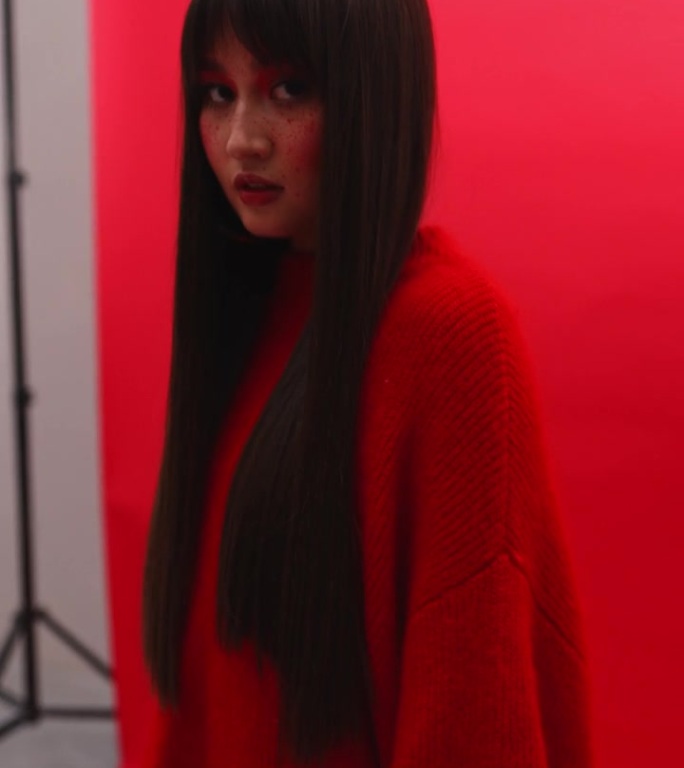 穿着高跟鞋和红色连裤袜的腿，镜头在亚洲女孩的脸上平移，在工作室里看着红色背景的相机。艺妓穿着红色的衣