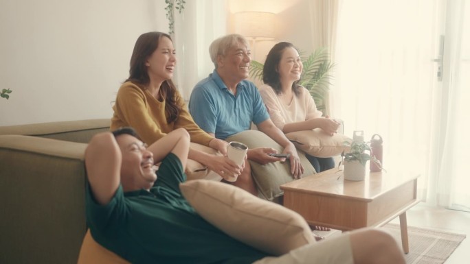 优质的家庭时刻:快乐的亚洲父母和十几岁的女孩在舒适的客厅一起看电视。
