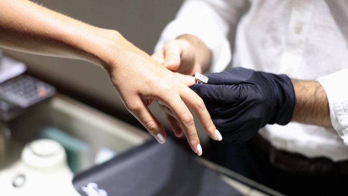 戴手套的珠宝商把戒指戴在女人的手指上
