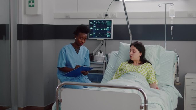 生病的女人躺在床上，而非裔美国护士在监测病情
