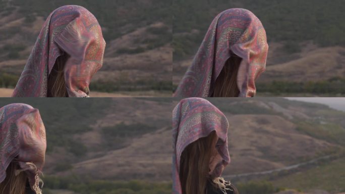 一个孤独的女人，脸上围着围巾，背景是夕阳下的山景。风试图吹走围巾，释放个性。心理状态的视觉表现
