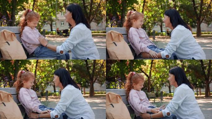 老妇人蹲在公园外面的长椅上和孙女聊天。