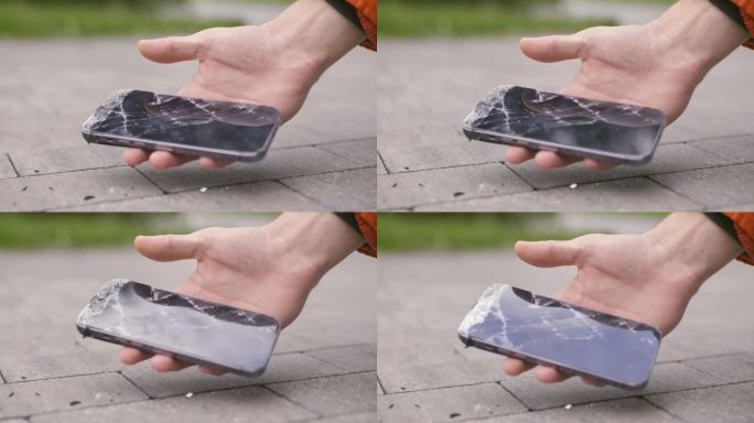 智能手机在人行道上摔了一跤，一名男子拿着一个坏了屏幕的智能手机捡了起来