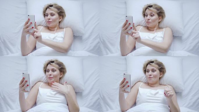 心情激动的女人躺在舒适的床上，用智能手机看最喜欢的电视剧或最喜欢的乐队的在线演唱会，睡眠问题