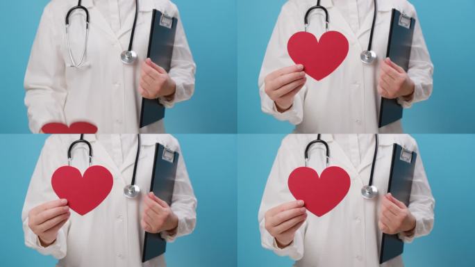 不知名女医生的特写，穿着制服，听诊器拿着红色的心脏形状，孤立在蓝色背景上。爱，捐赠，世界心脏日，世界