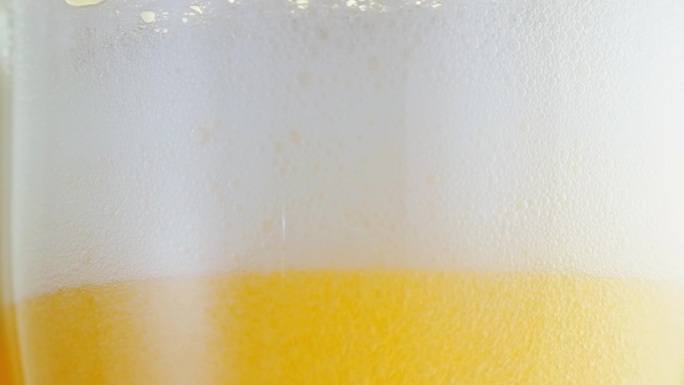 啤酒在啤酒杯中，形成冒泡的气泡和泡沫的头部。啤酒泡沫顺着玻璃杯流下细节拍摄，微距拍摄。啤酒抓住了十月