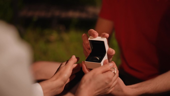 特写镜头。男性的手打开装有结婚戒指的盒子。女人的手轻轻地抱着男人的手，手里拿着一个盒子。