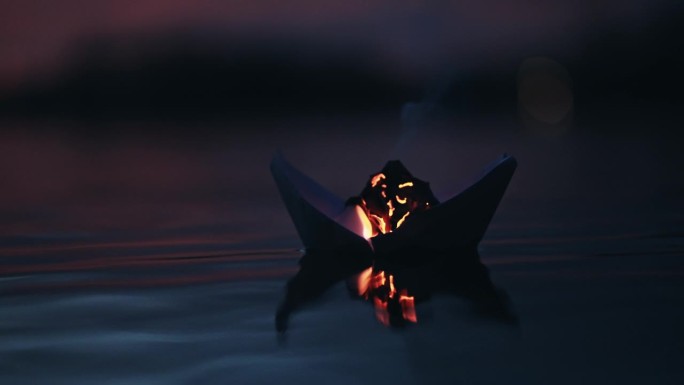 燃烧的折纸船漂浮在湖面上，在暮色中泛起涟漪