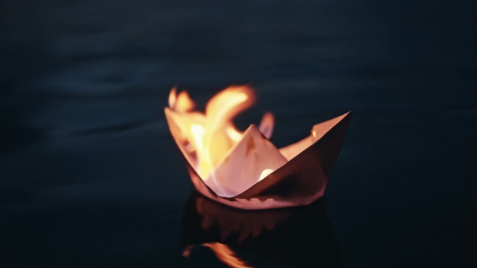 夜间漂浮在河上燃烧的折纸船的高角度特写