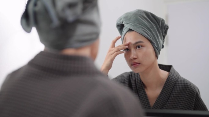 一名亚洲妇女正对着浴室的镜子检查脸上的瑕疵和粉刺，准备洗澡。捕捉日常护肤和自我护理的时刻，为容光焕发