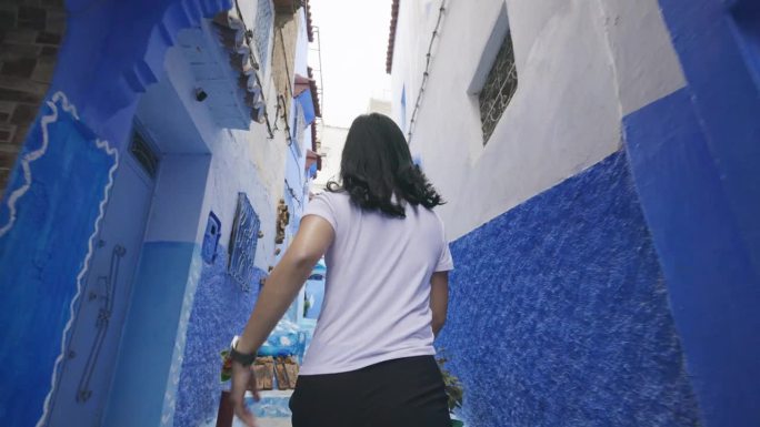 一名无法辨认的女游客在探索摩洛哥舍夫沙万的蓝色城市时的后景