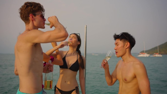 一群不同的朋友在游艇上开派对，喝着香槟。迷人的年轻男女聚在一起，庆祝节日，双体船在夏日夕阳下航行。
