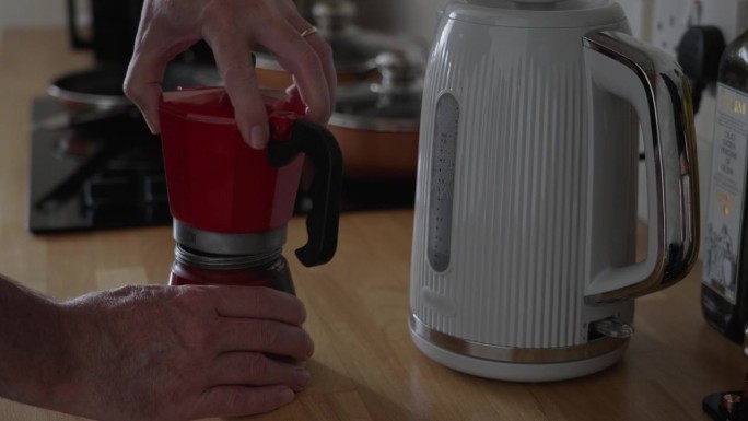 手拧开一个红色的炉子，把浓缩咖啡壶放在厨房的木制柜台上