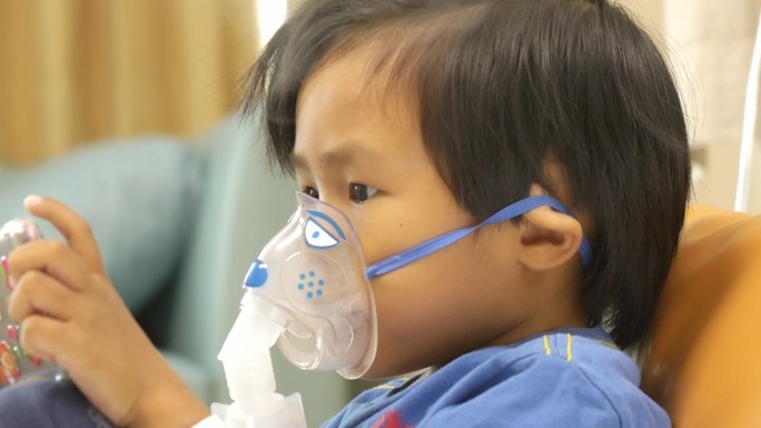 亚洲男孩在医院一边玩手机游戏一边使用吸入器。