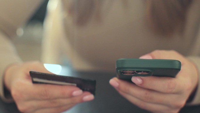 妇女手持智能手机和信用卡在家里网上购物的特写。智能手机购物网银服务理念。