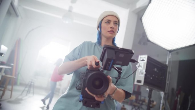 慢镜头的女电影摄影师工作在一个拍摄集，使用数码相机拍摄高质量的镜头为电影项目。有创意的女人操作照相机