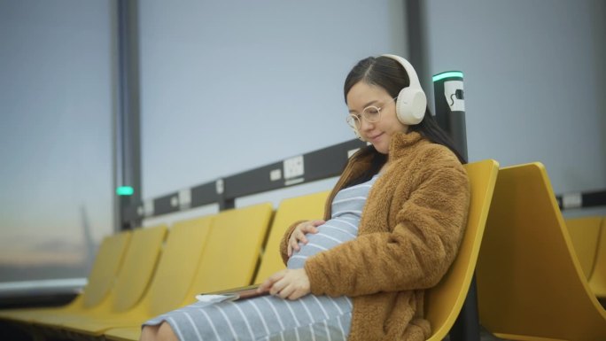 穿着考究的孕妇在机场候机时听着音乐摸着肚子