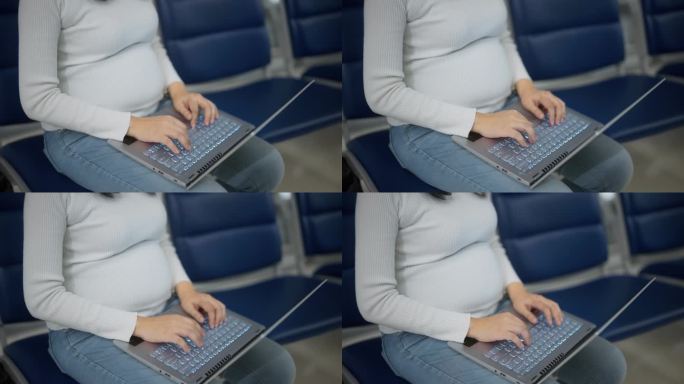 孕妇在机场候机时揉着肚子玩着笔记本电脑