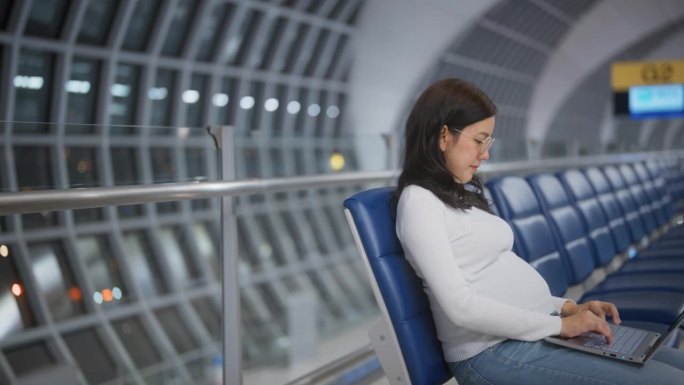 一位孕妇在机场候机时坐着使用笔记本电脑