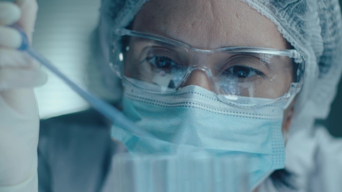 戴防护口罩的女实验室技术员往试管里滴液