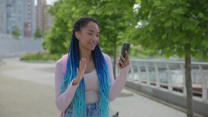 留着脏辫的年轻非裔美国女人在城市里走来走去打视频电话