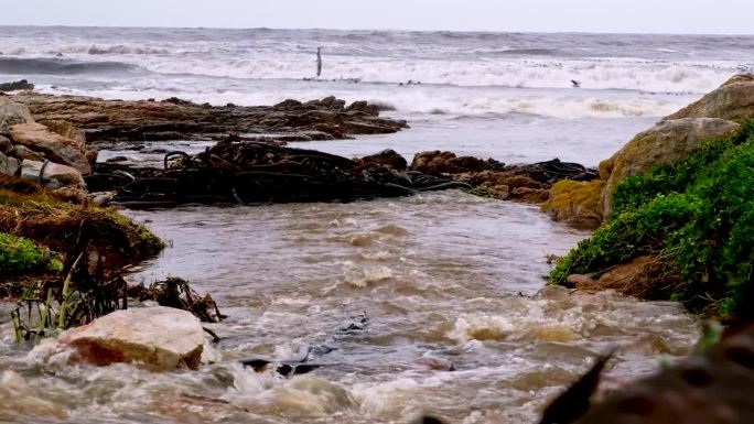 浑浊的雨水从排水系统流入海岸线上波涛汹涌的大海