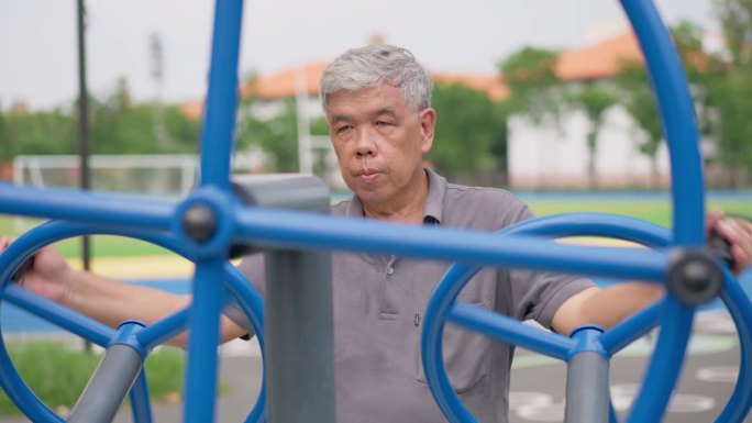 一位年长的亚洲男子在公园的健身站随意锻炼。代表以运动永葆青春，露天健身，身体健康的理念。城市公园户外